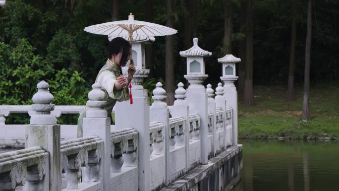 穿着旗袍的美女撑伞在石栏水边赏鱼