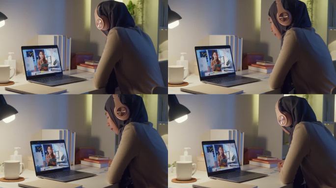 年轻快乐的亚洲穆斯林女秘书戴着头巾，穿着休闲服，在笔记本电脑上与女商人在家进行视频会议，晚上加班。在