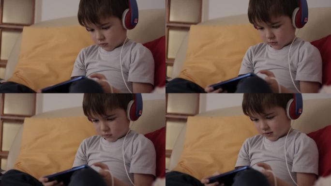 孩子玩手机玩得很开心。小男孩戴着耳机在手机上玩电子游戏。学龄前儿童在智能手机上玩视频游戏。对儿童心理