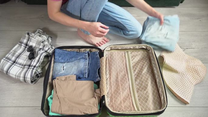 一个人把他的手提箱装上一叠钱准备长途旅行。盖上绿色的行李箱，手提行李里的衣服拉上拉链。旅游者为旅行打