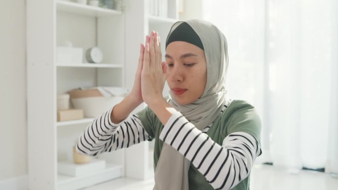 特写亚洲穆斯林妇女穿着穆斯林运动服做瑜伽初学者练习视频在线课程训练从笔记本电脑在家里的客厅。伊斯兰保