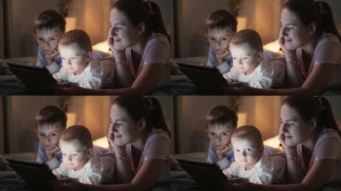两个男孩在睡觉前在平板电脑上看视频的幸福家庭。家人聚在一起，养育孩子，看视频，上床睡觉