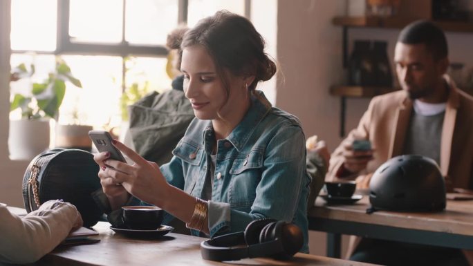 美女在咖啡馆用智能手机发短信，在社交媒体上分享信息，享受移动技术，在繁忙的餐厅等待