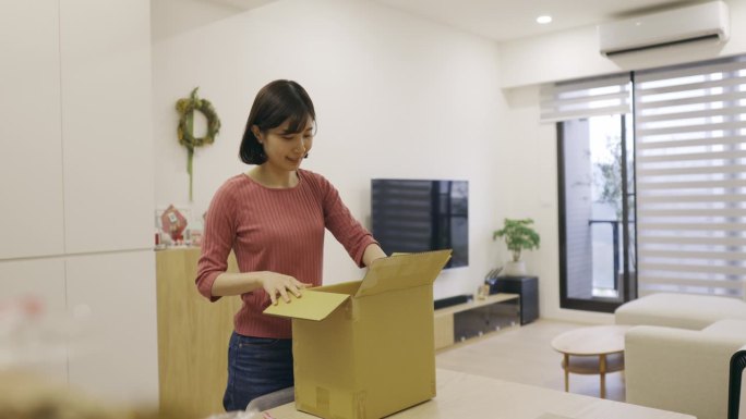 亚洲女性在家里收到包裹，打开并确认购买的物品。