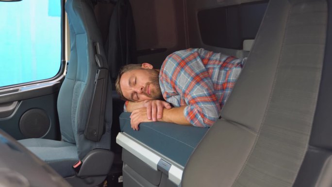 卡车司机在长途加班后睡在他的小屋里。昏昏欲睡的卡车司机在卡车运输车的床上打盹。睡眠不足