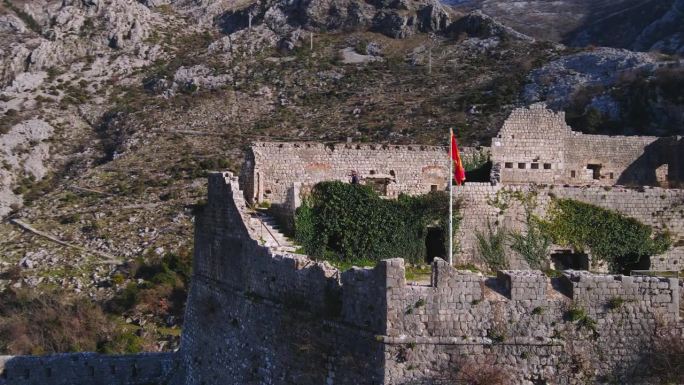 无人机镜头捕捉到了科托尔堡垒令人惊叹的景色，上面飘扬着黑山红旗。航拍画面展示了这座堡垒复杂的设计和优