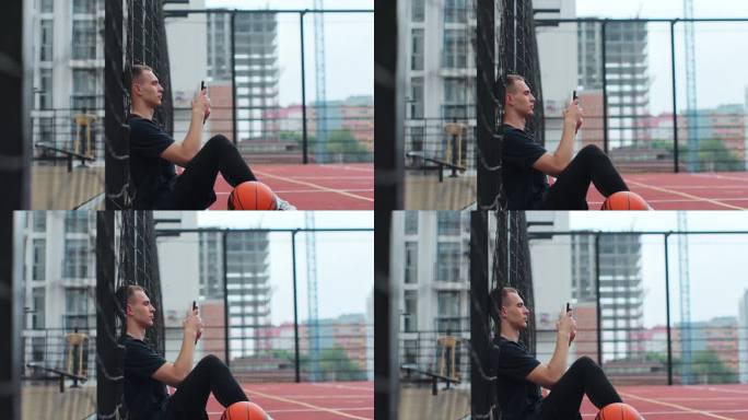侧视图，年轻的运动男子坐在篮球场上，滚动智能手机，使用应用程序。在户外运动场上休息。爱好、运动、生活