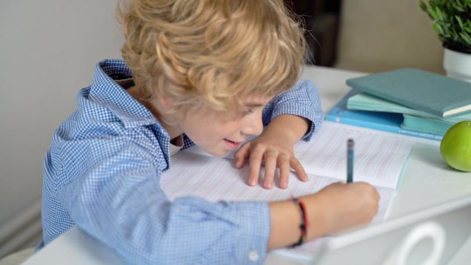 小学生男孩或女孩写信，在课桌上学习。回到学校，白色背景。第一课，字母表，小学生知识。广告文案空间。
