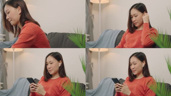 幸福的亚洲女人用手机听音乐，无线耳机放松在家里客厅的沙发上