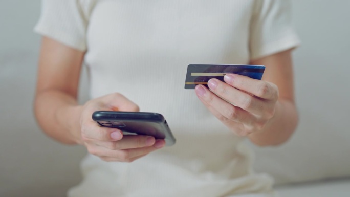 年轻的休闲女商人拿着信用卡，用触屏智能手机在咖啡馆里点餐，进行网上购物。商业、生活方式、科技、电子商