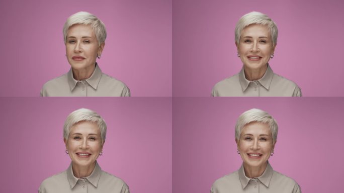 在彩色工作室拍摄的成年妇女看着相机微笑的肖像。孤独的老年女性粉红色背景特写。上了年纪的人，涂着时髦的