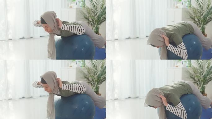 运动的伊斯兰妇女穿着穆斯林运动服，打普拉提运动球，在瑜伽垫上锻炼肩部肌肉，在家里客厅的笔记本电脑上进