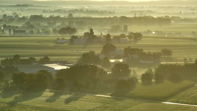清晨日出时，美国乡村农田上的雾气、薄雾和露水。玉米田、农场、谷仓、筒仓和树木的空中拍摄。