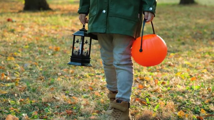 一个男孩带着万圣节的南瓜桶和灯笼走在秋天的森林里。