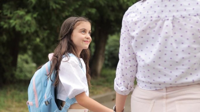 一个快乐的女孩背着书包上学，牵着妈妈的手。在学校学习