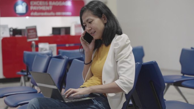 年轻的亚洲商务女性在国际机场候机楼门口等待航班起飞时，用手提电脑检查出差计划和航班时刻表，确认与同事
