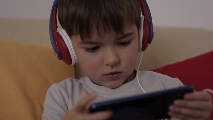 孩子玩手机玩得很开心。小男孩戴着耳机在手机上玩电子游戏。学龄前儿童在智能手机上玩视频游戏。对儿童心理