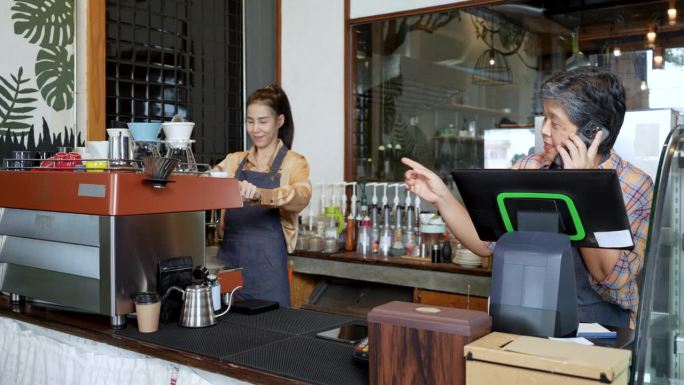 小型企业;咖啡店老板妈妈在电话上接顾客的订单，咖啡师女儿在咖啡机上，微笑着开心地接到了很多订单。