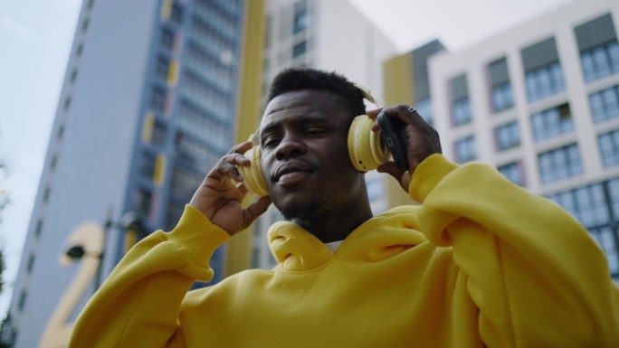 非裔美国音乐爱好者走在城市街道上，戴着耳机听着最喜欢的歌曲