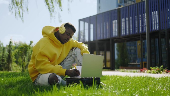 黑人男学生在线学习，独自坐在公园里使用现代电子设备进行交流