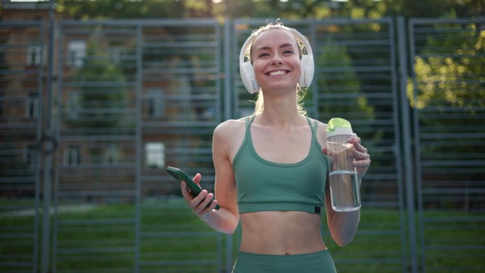 漂亮的效果愉快的无忧无虑的女性慢跑者享受健康的生活方式和户外跳舞，同时从智能手机小工具应用程序听积极
