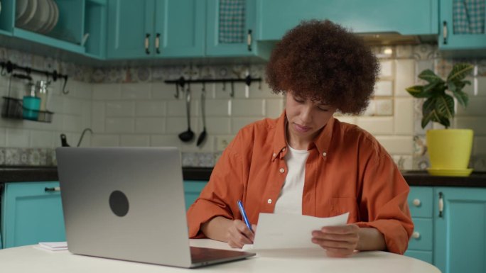 黑人女性用笔记本电脑打字，30多岁的企业家，在家办公室管理文件、发票、税单。