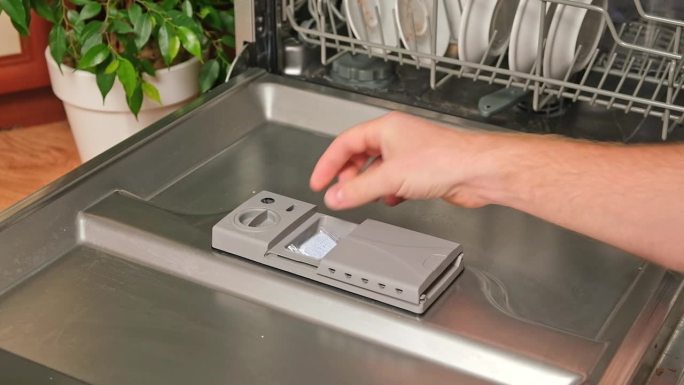 把平板电脑放进洗碗机。一个男人把平板电脑放在洗碗机里洗脏盘子。