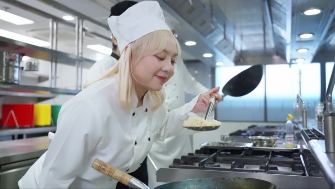 中国女厨师闻着传统泰式炒饭，用翻锅技术提高食物的气味和味道，微笑的高级厨师指导老师对她的厨师学生成绩