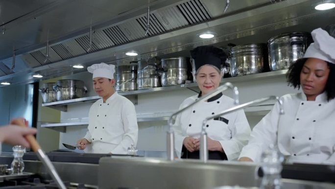 在高级厨师指导下，厨师在餐厅厨房用炒锅和锅铲准备炒菜，女厨师指导指导多种族厨师准备炒菜