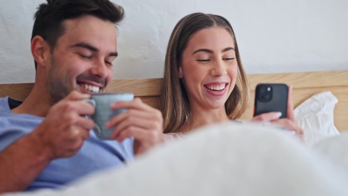 情侣，在床上喝咖啡和打电话，在度假的早晨为表情包、帖子或网络博客微笑和滑稽大笑。男人、女人和智能手机
