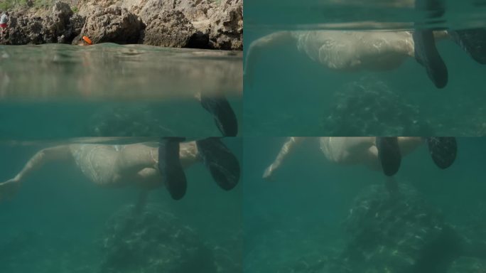 摄像机下降到水下，捕捉到一个戴着浮潜面具的年轻女子在海面上游泳，看着海底的岩石。