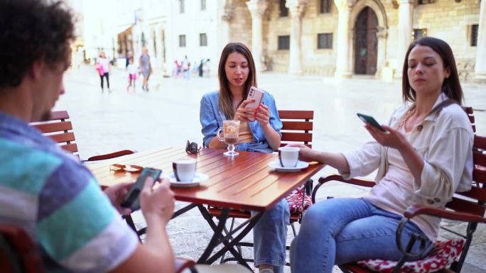 三个朋友坐在镇上的咖啡店里喝咖啡，刷社交媒体