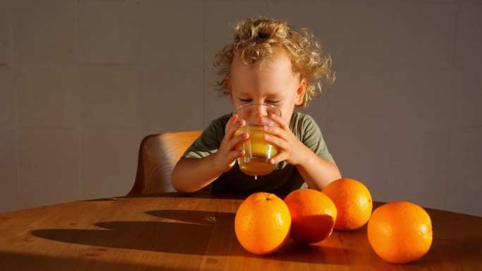 男孩拿起一杯橙汁，抿了一小口，眯着眼睛看着那酸甜的味道。