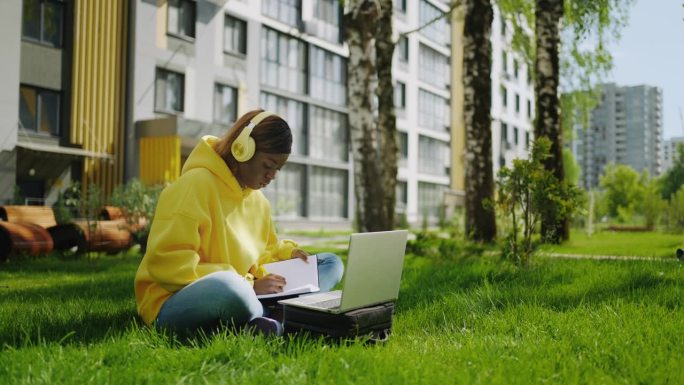 年轻的黑人女性通过笔记本电脑在线学习，使用无线耳机听声音