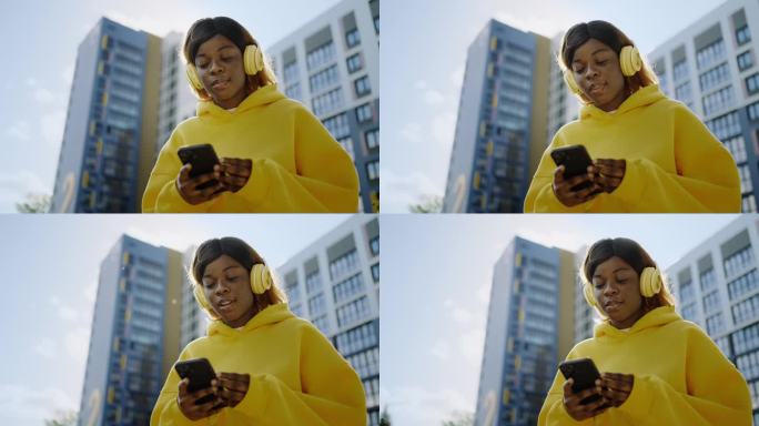 黑人妇女在街上用智能手机和耳机的中等肖像，非洲女孩使用应用程序