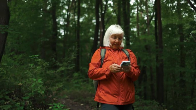 高级女徒步旅行者在森林里享受周末时使用智能手机。低角度的视角，有吸引力的老妇背包客规划行程路线在森林
