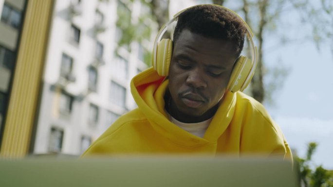 聪明的非洲裔美国人戴着耳机在公园里看笔记本电脑的展示，特写