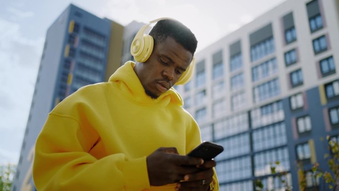 年轻的非裔美国男性在城市街道上使用智能手机和无线耳机