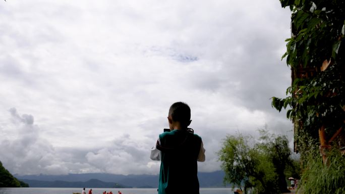 小男孩在泸沽湖里格半岛上拍摄湖中游船