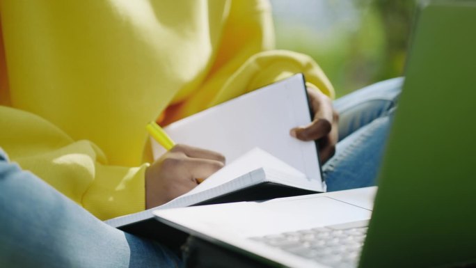 黑人女性用笔记本和笔记本电脑写字的手特写，在线教育