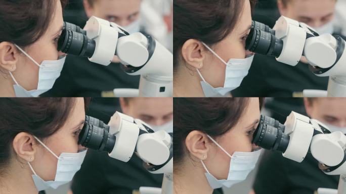 一位女医生在显微镜下近距离观察。女科学家在双筒显微镜下的侧视图