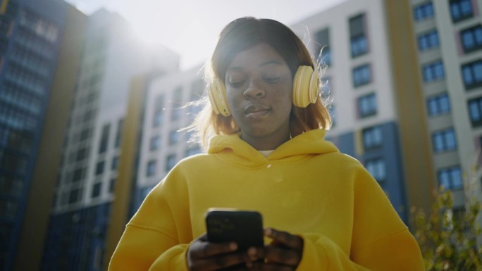 年轻的黑人女性社交媒体用户站在街上用智能手机上网