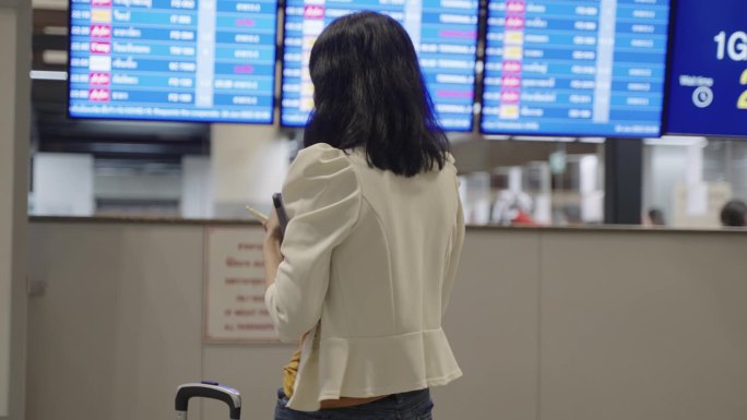 年轻的亚洲商务女性在国际机场候机楼门口检查商务旅行计划和航班时间表，确认与同事的会议文件。