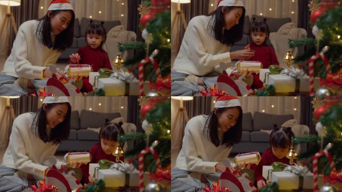 亚洲年轻快乐的家庭晚上在家里一起享受新年假期聚会。妈妈和孩子一起把礼品盒放在圣诞树旁装饰。度假的生活