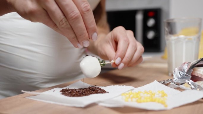 一位糕点师正在制作巧克力草莓，她在白巧克力上撒上红糖装饰。