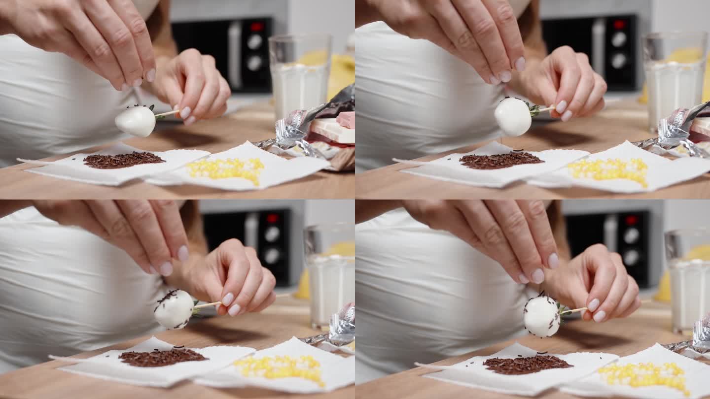 一位糕点师正在制作巧克力草莓，她在白巧克力上撒上红糖装饰。