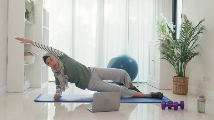 运动亚洲伊斯兰妇女穿着穆斯林运动服锻炼伸展腿和流动手臂初学者练习在线课程训练从笔记本电脑在家里的客厅