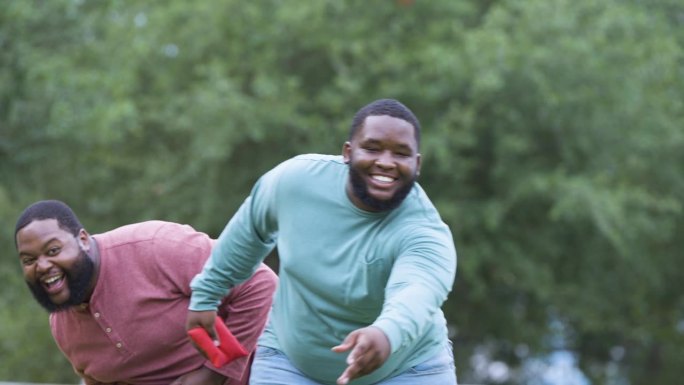 两个魁梧的黑人在玩掷豆袋游戏，笑着