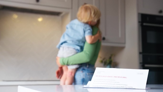 母亲抱着儿子在家里，柜台上有关于抵押贷款利率提高的信