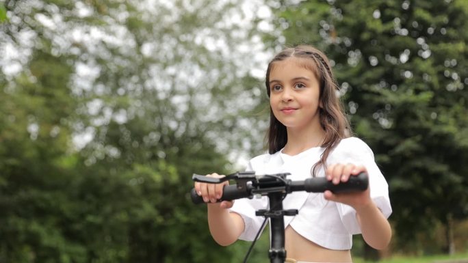 一个小女孩正在学习骑电动滑板车。在城市公园里骑摩托车。体育生活